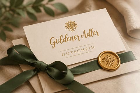 Graphic illustration of a voucher on paper with a green ribbon and wax seal featuring the Goldener Adler logo